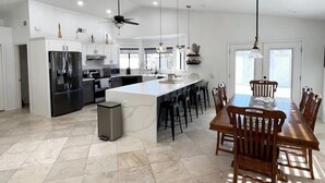 A modern kitchen with a central island, white cabinetry, and a dining area with wooden chairs.