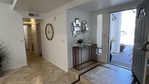 A spacious hallway with a tiled floor, a clock on the wall, and a door leading outside.