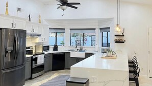 A modern kitchen with a large island, stainless steel appliances, and a ceiling fan.