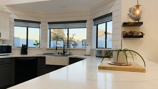 A modern kitchen with a large island, black appliances, and a view of the outdoors.