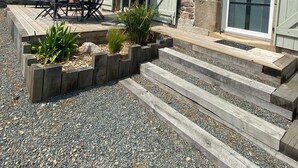 A stone house with a patio, outdoor seating, and a large sliding glass door. - Maison AU Calme (Ploëzal)