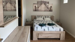 A bedroom with a bed, bedside tables, a nightstand, a mirror, and a hanging light fixture. - Maison AU Calme (Ploëzal)