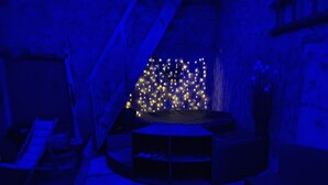 A room with a stage area featuring a backdrop of small lights, a seating arrangement with chairs, and a staircase in the background. - Maison AU Calme (Ploëzal)
