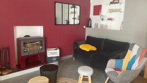 A living room with a red wall, a black sofa, a wooden coffee table, a grey armchair, and a small wooden stool. - Maison AU Calme (Ploëzal)