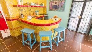 A kitchen with a yellow and red tiled backsplash, a sink, a stove, and two blue stools. - Mexican flair One Bedroom (Puerto Vallarta)