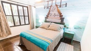 A bedroom with a bed, a nightstand, a wall mural, and a window. - Mexican flair One Bedroom (Puerto Vallarta)