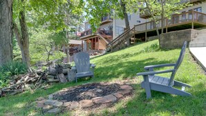 Ein Garten mit Feuerstelle, zwei Adirondack-Stühlen, einer Holzterrasse und einer Treppe zu einem Gebäude mit Balkon.