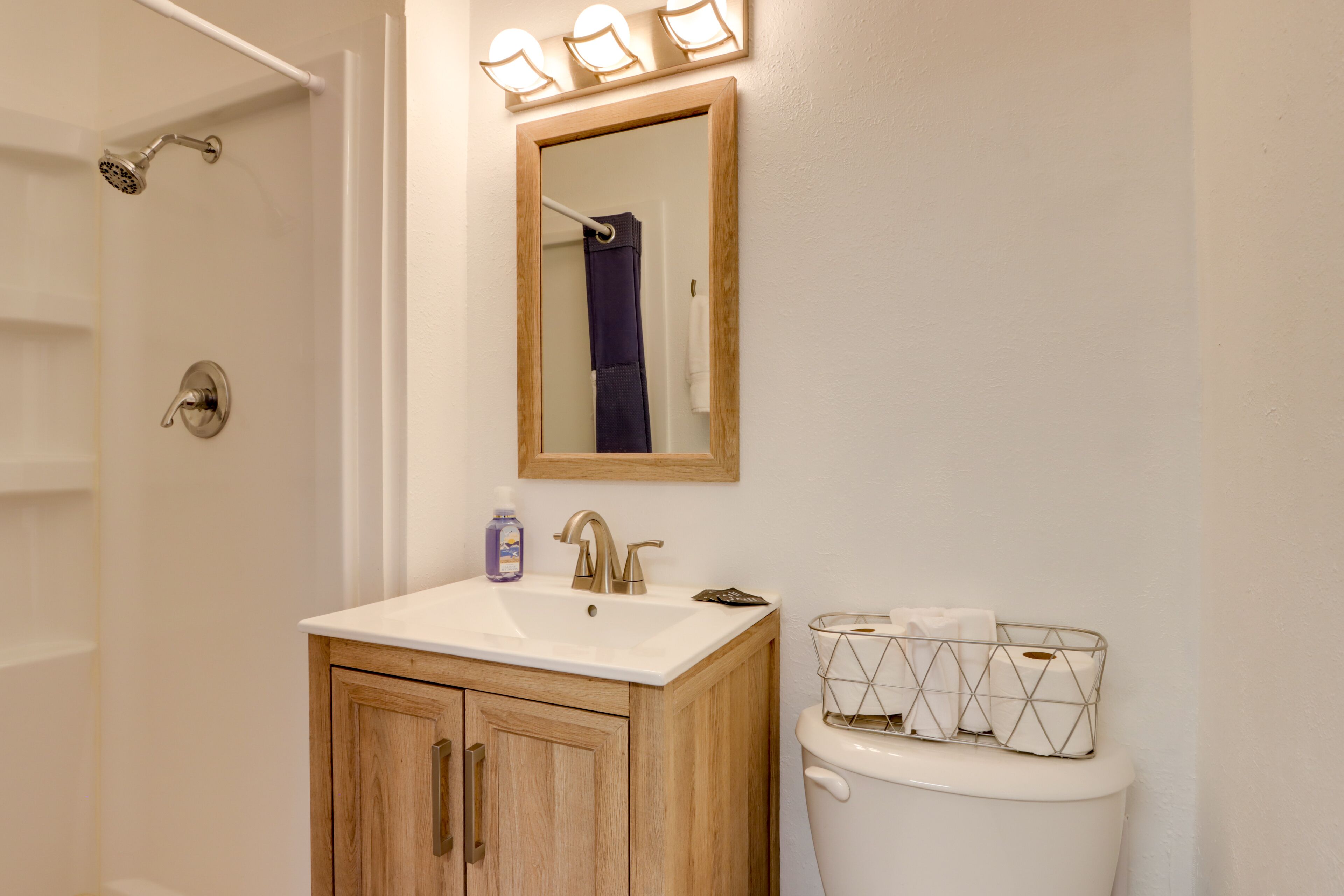 Een badkamer met een houten kastje, een wit wastafel, een spiegel en een toilet met een houder voor tissues.