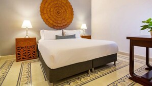 A neatly made bed with a white comforter and two pillows, flanked by two nightstands with lamps, a decorative wall piece, and a small table with a plant. - L1-CM APARTAMENTO TIPO LOFT EN GETSEMANI (Cartagena)