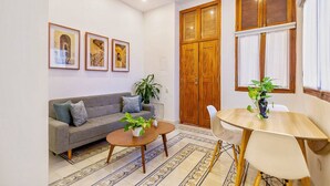A living room with a sofa, coffee table, and a dining table with chairs. There are framed pictures on the wall, a large wooden door, and a window with curtains. - L1-CM APARTAMENTO TIPO LOFT EN GETSEMANI (Cartagena)