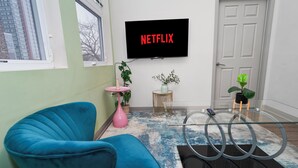 A living room with a blue chair, a pink vase, and a TV displaying 'NETFLIX'.