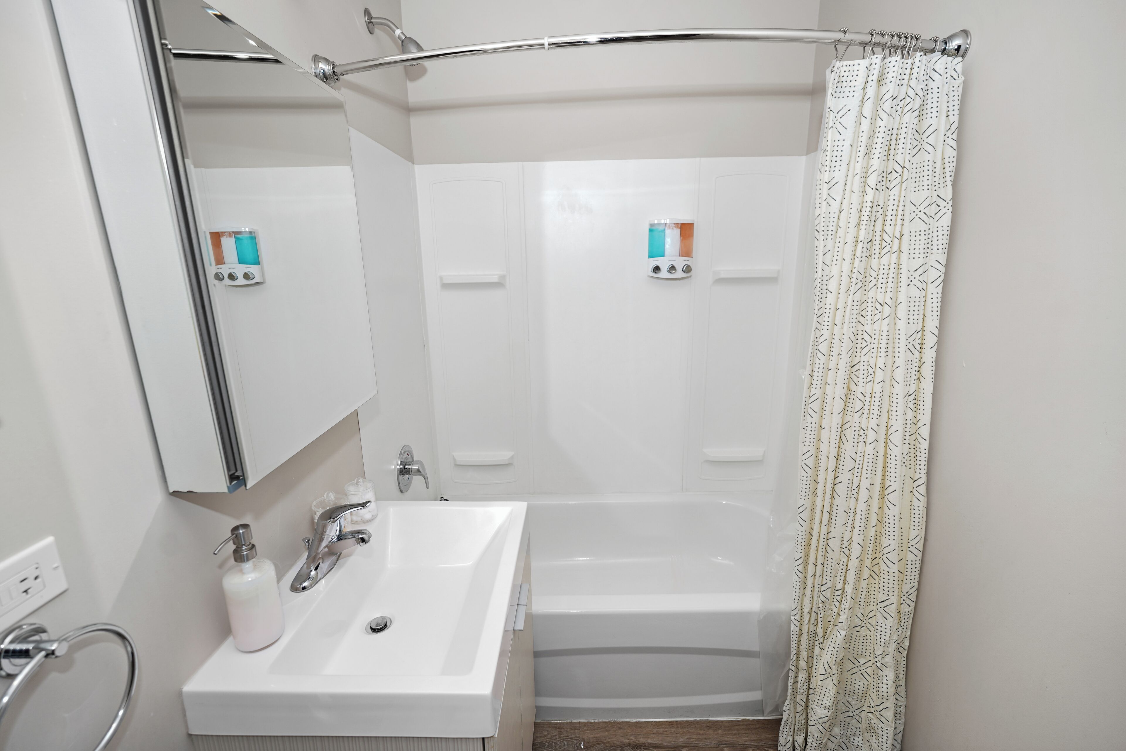 Un baño moderno con lavamanos blanco, una bañera y un cortinero de ducha.
