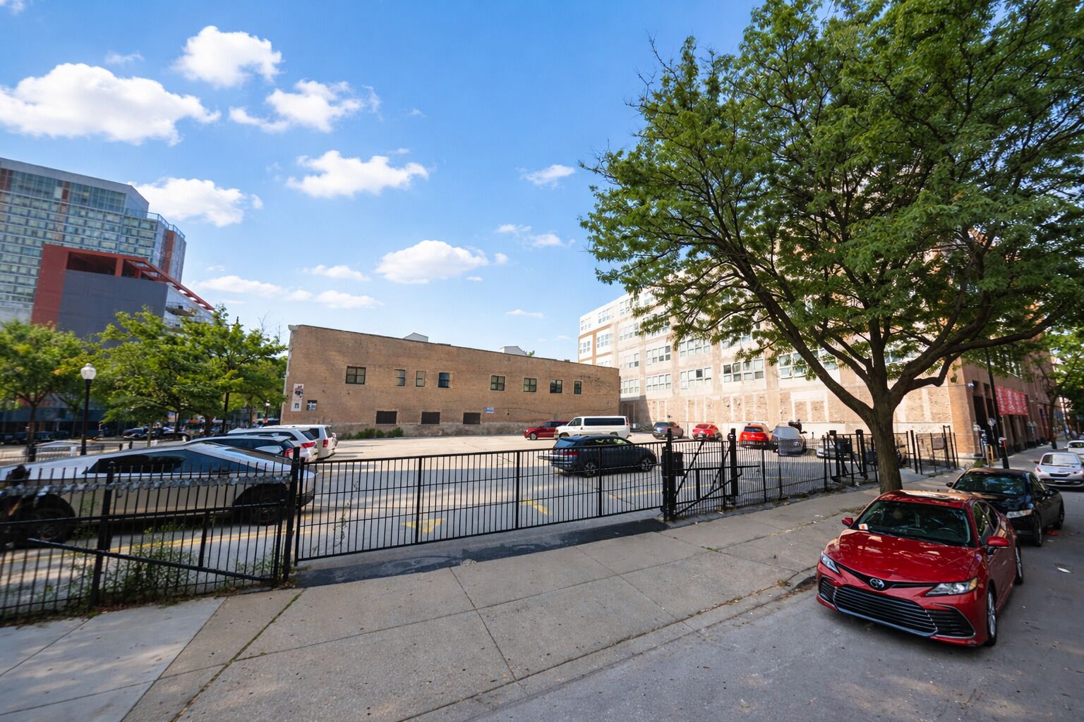 A parking lot with cars, a fence, and buildings in the background.