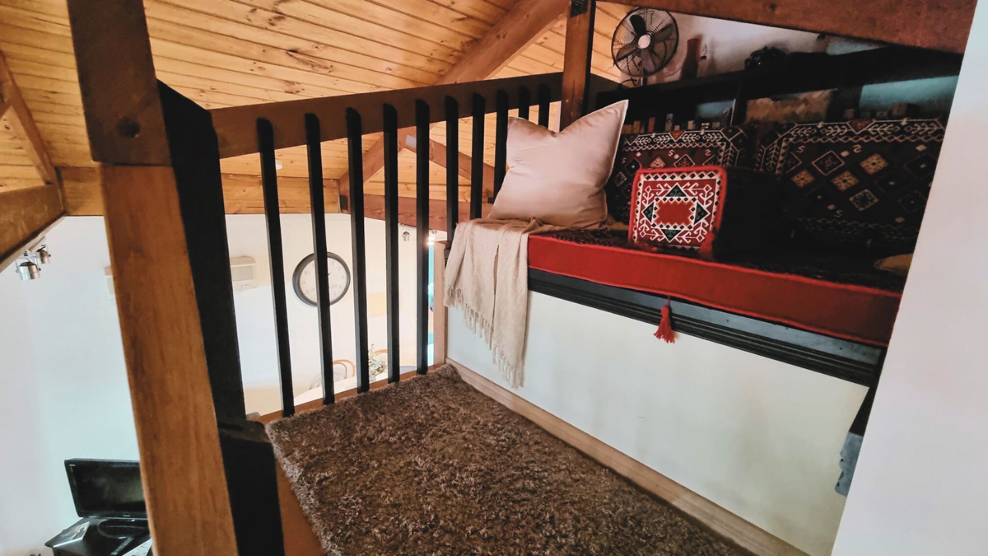 A wooden staircase with a handrail, a red and white bench with patterned cushions, and a clock on the wall.