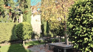 Un jardin avec une table et des chaises, une haie et un arbre.