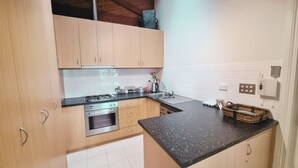 Une cuisine compacte avec des meubles en bois, une cuisinière à gaz, un four encastré, un évier et un plan de travail noir.