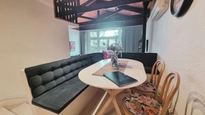 Un comedor con una mesa redonda, un banco acolchado negro y sillas de madera.
