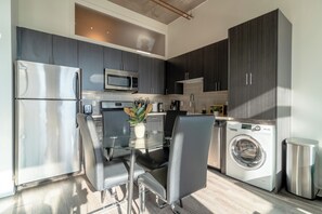 A modern kitchen with stainless steel appliances, a glass dining table, and dark cabinetry. - McCormick Place city view 2br/2ba with optional parking for up to 8 guests (Chicago)