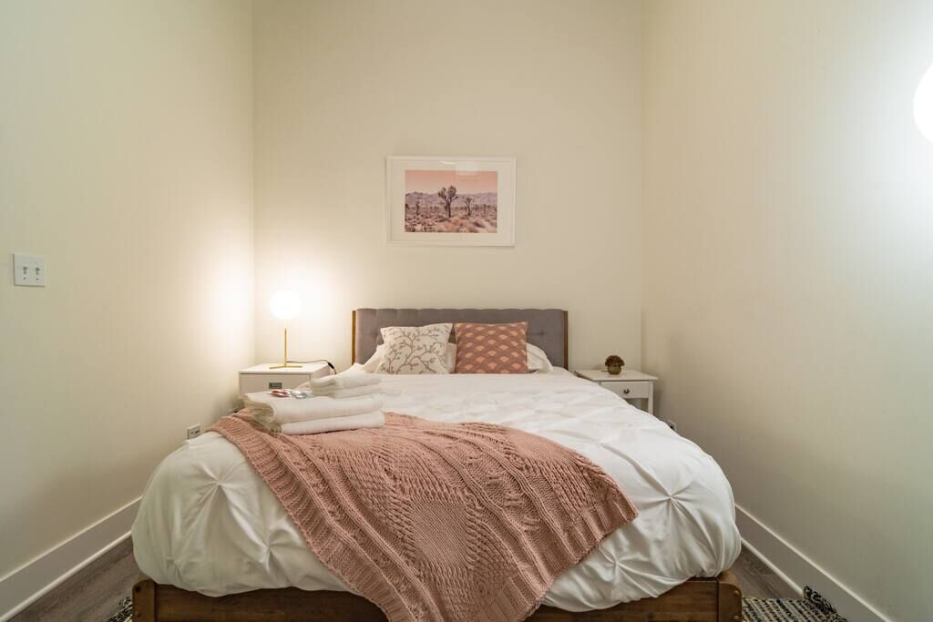 A neatly made bed with a pink blanket, a bedside lamp, and a framed picture on the wall.