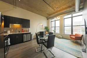 A modern kitchen with dark cabinets, stainless steel appliances, and a dining area with a glass table and black chairs.