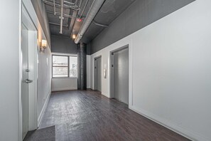 A hallway with a dark wooden floor, white walls, and a ceiling with exposed pipes and lighting fixtures. - Stylish 2BR South Loop Family Unit Near McCormick Place & Soldier Field (Chicago)