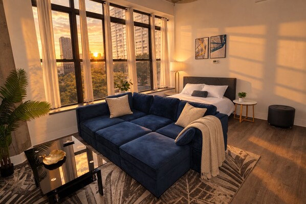 A modern bedroom with a large bed, a blue sofa, and a city view through large windows.