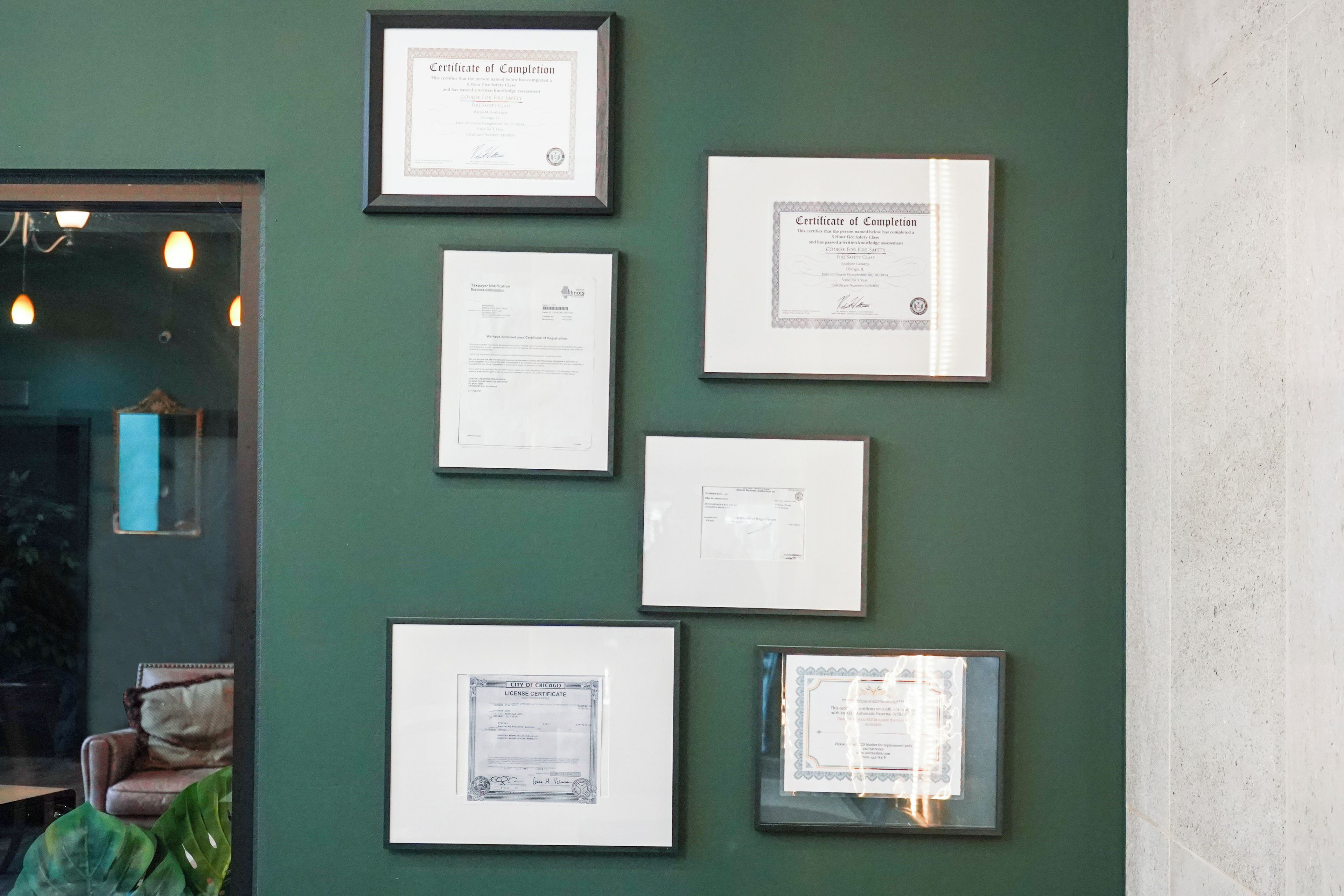 A wall with multiple framed documents, including certificates and a license certificate.