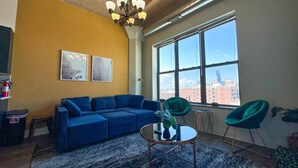 A modern living room with a blue sectional sofa, a round coffee table, and a large window offering a city view.