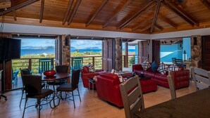 Uma sala de estar ampla com teto de madeira, sofás vermelhos e vista para o mar.