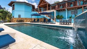 Uma área de piscina com uma cascata, espreguiçadeiras e um espaço de estar coberto.