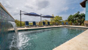 Piscina com cascata, espreguiçadeiras e guarda-sóis.