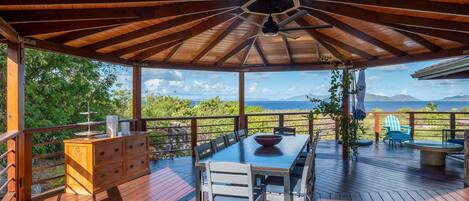 Une terrasse extérieure avec une table et des chaises en bois, un meuble en bois et une vue sur l’océan.