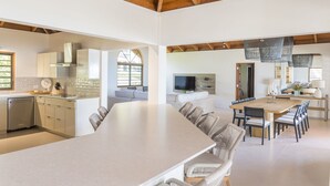 A spacious kitchen with a large island, modern appliances, and a dining area with a long table and chairs. - Sea Palms Villa - Holiday in Luxury in this Stunning Rental Villa (Mahoe Bay)