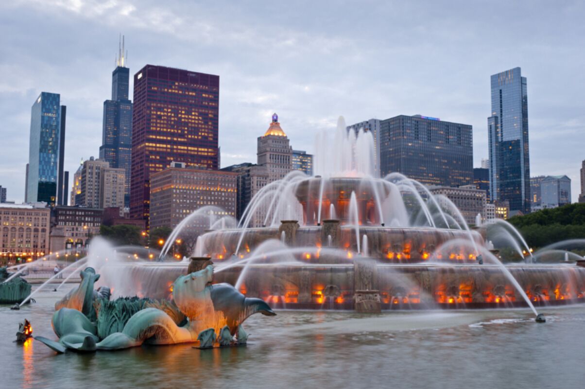 Une vue urbaine mettant en valeur une fontaine imposante, avec de nombreux jets d’eau et des sculptures au premier plan.