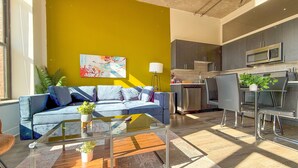 A modern living room with a sofa, coffee table, and a dining area with chairs and a small kitchen in the background.