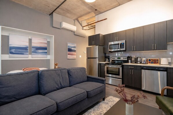 A modern kitchen with dark cabinets, stainless steel appliances, and a grey sofa in the living area. - McCormick Place Studio with optional parking for up to 4 guests (Chicago)