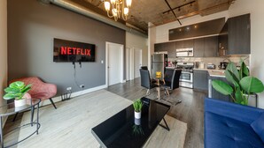 A modern living room with a flat-screen TV, a black coffee table, and a blue sofa. - McCormick Place Patio skyline 2b/2b with optional Parking for up to 6 people (Chicago)