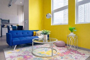 Una sala de estar moderna con un sofá azul, una mesa de centro de vidrio y una pared de acento amarilla.
