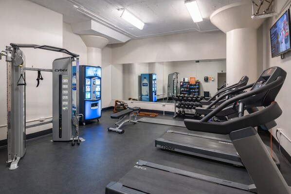 Un gimnasio con cintas de correr, máquinas de pesas y una pantalla Cybex.