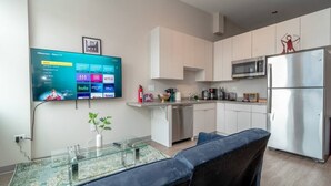 Una cuina moderna amb armaris blancs, un frigorífic d'acer inoxidable i un televisor de pantalla plana muntat a la paret que mostra serveis de streaming.