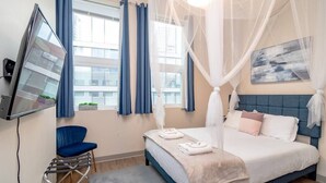A bedroom with a bed, a chair, a TV, and a window with curtains.
