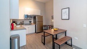 A modern kitchen with white cabinets, stainless steel appliances, and a wooden dining table with benches.