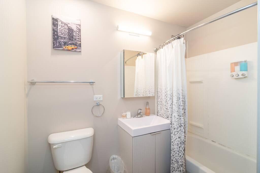 A bathroom with a toilet, sink, shower, and a mirror.