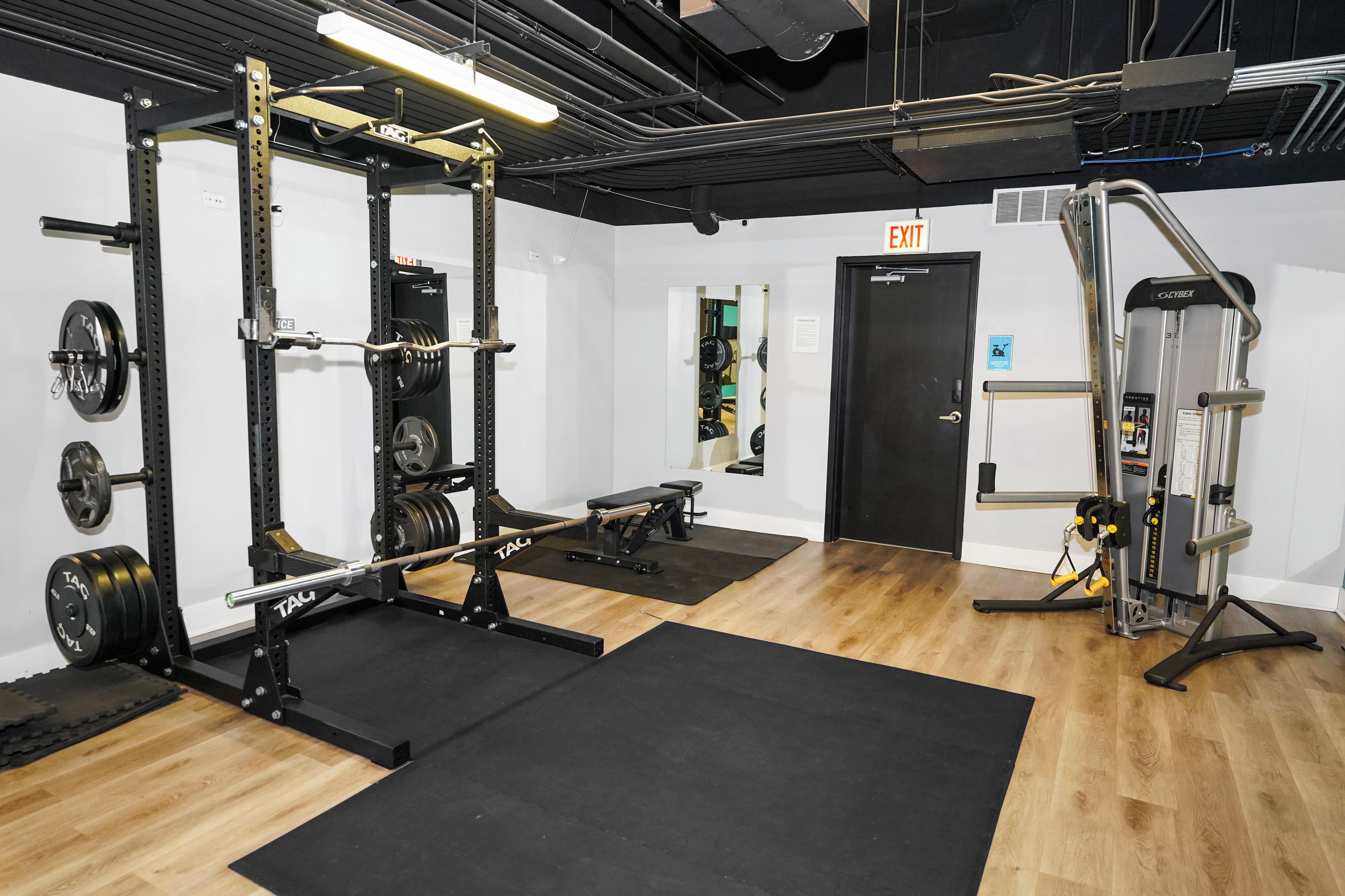 Un gimnasio con equipamiento de levantamiento de pesas, una banca y una puerta señalizada con 