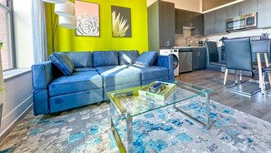 A modern living room with a blue sofa, a glass coffee table, and a vibrant green accent wall.