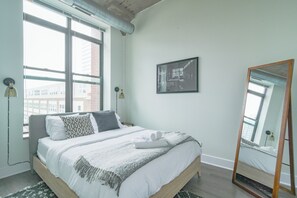 A bedroom with a bed, a large window, a mirror, and a framed picture on the wall. - McCormick Place 2b/2b family unit with optional parking for up to 8 guests (Chicago)