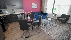 Une cuisine moderne avec des meubles de couleur sombre, un coin repas doté d’une table en verre et un salon avec un canapé bleu.