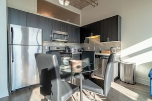 A modern kitchen with stainless steel appliances, dark cabinetry, and a glass dining table with chairs.
