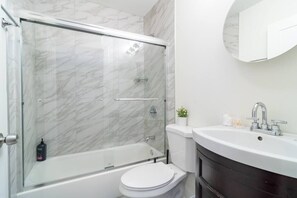 Ein Badezimmer mit einer gläsernen Duschkabine, einer weißen Toilette, einem dunklen Holzwaschtisch und einem weißen Waschbecken mit Spiegel darüber.