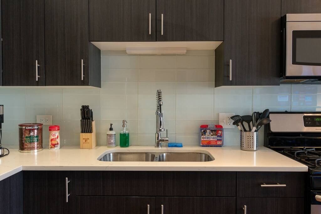 Una cocina moderna con armarios oscuros, un lavamanos de acero inoxidable y un microondas.